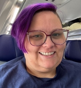 Person smiling with short purple hair and glasses