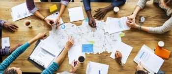 aerial view of diverse group of people in a planning meeting around a wood table covered with various papers