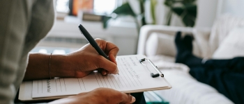 Photo of a persons' hand filling out a paper on a clipboard